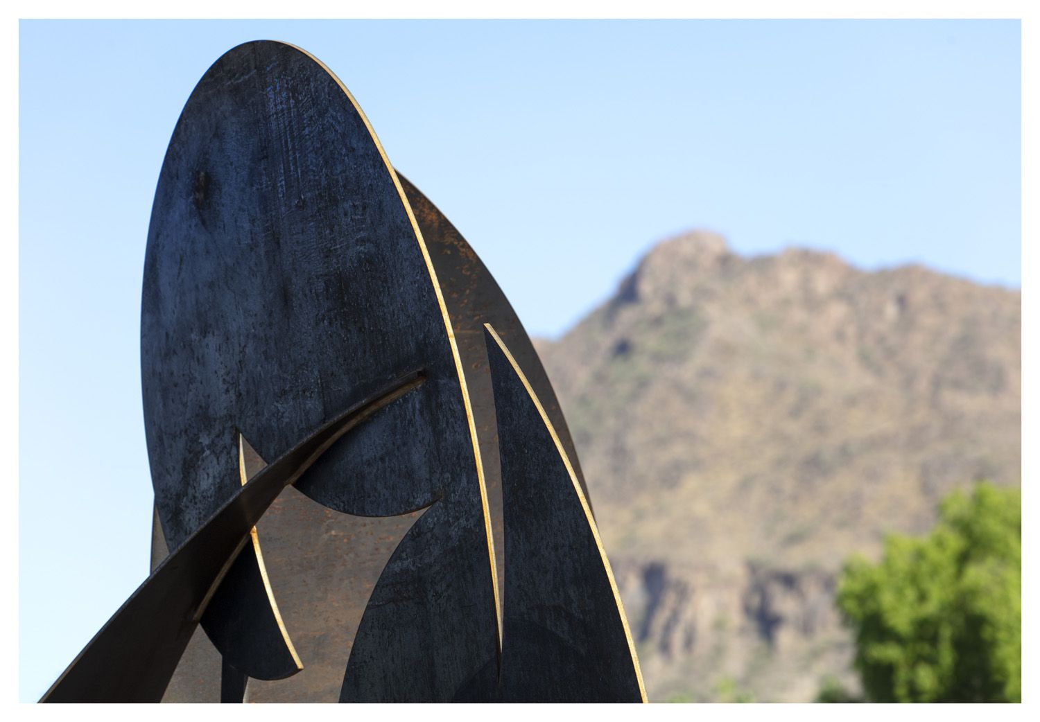Abstract metal sculpture art set against a mountain and clear blue sky, inspiring creativity in the community.