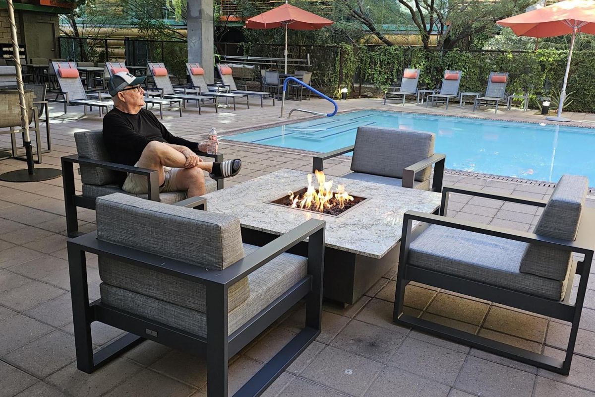 Resident Stories: Bob McMillan enjoys a cozy evening by the fire pit at Optima Sonoran Village with poolside views and orange umbrellas.