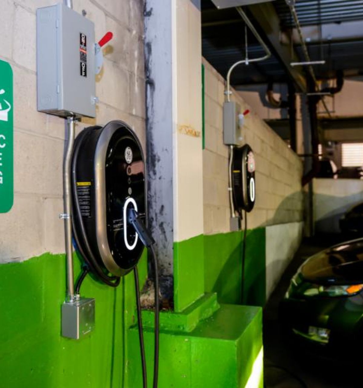 Electric vehicle charging stations in a parking garage, with EVs parked and charging nearby.