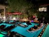 People relaxing on floating mats in a pool at night during Optima Communities' celebration events, surrounded by candles and red umbrellas.