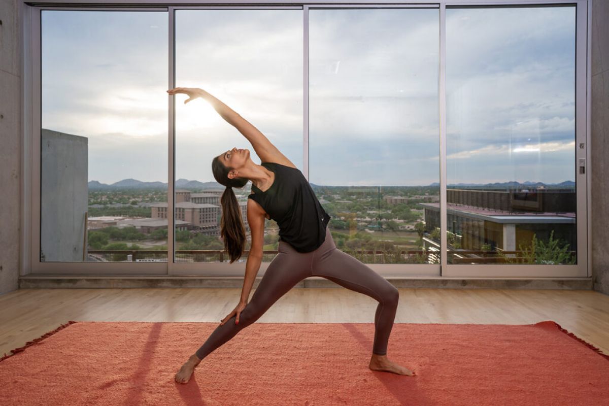 Woman practicing yoga in a modern room, focusing on mindfulness and stretching on a red mat with a scenic view behind her.