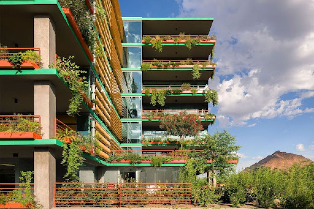 Modern apartment building with plant-filled balconies, embracing desert living against a blue sky and mountain backdrop.