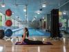Woman practices yoga in upward-facing dog pose by an indoor pool at Optima Sonoran Village, with Pilates balls nearby.