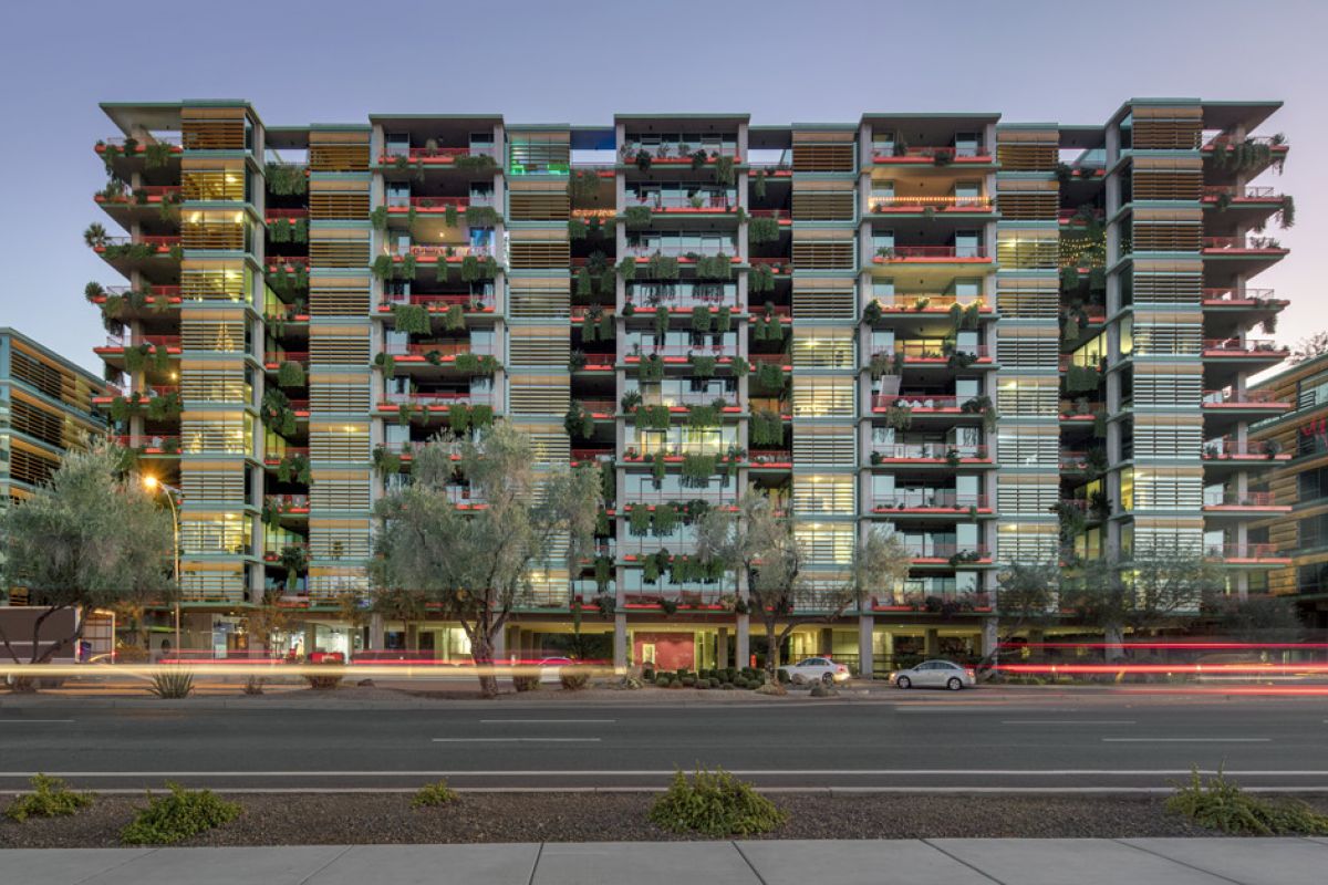 Modern multi-story apartment building at sunset, with balconies and greenery—Optima Sonoran Village blends climate design for the desert climate.