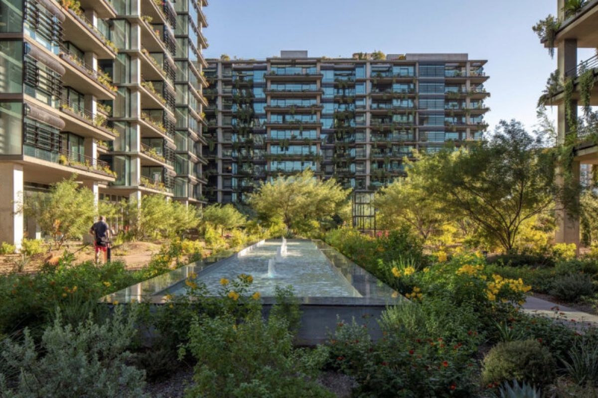 Modern apartment buildings with glass balconies, lush gardens, natural stone accents, and a long reflecting pool in the center.