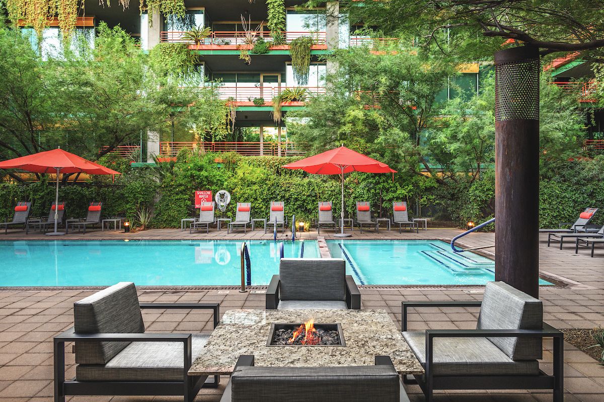 Modern poolside patio with red umbrellas, lounge chairs, and fire pit—perfect for Sky Deck evenings amid lush greenery in the background.