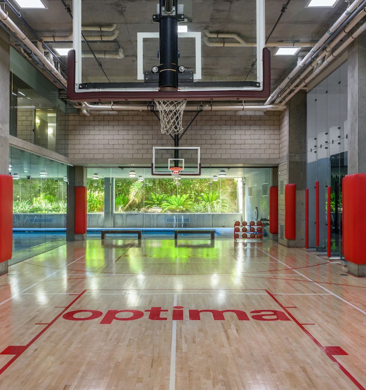 Indoor basketball court with “optima” on the floor and large windows—where spontaneous wellness meets sport amid lush green views.