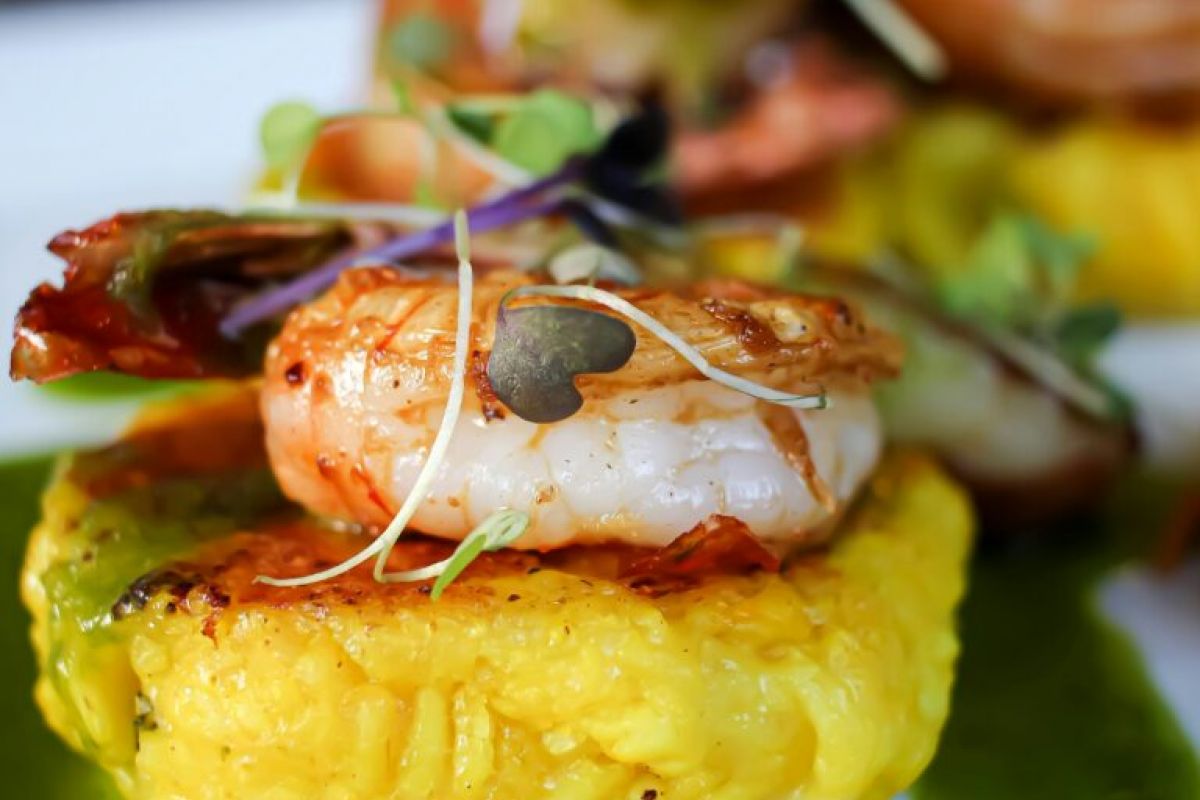 Grilled shrimp on yellow rice with microgreens and green sauce, plated on a white dish for Arizona Spring Restaurant Week 2024.