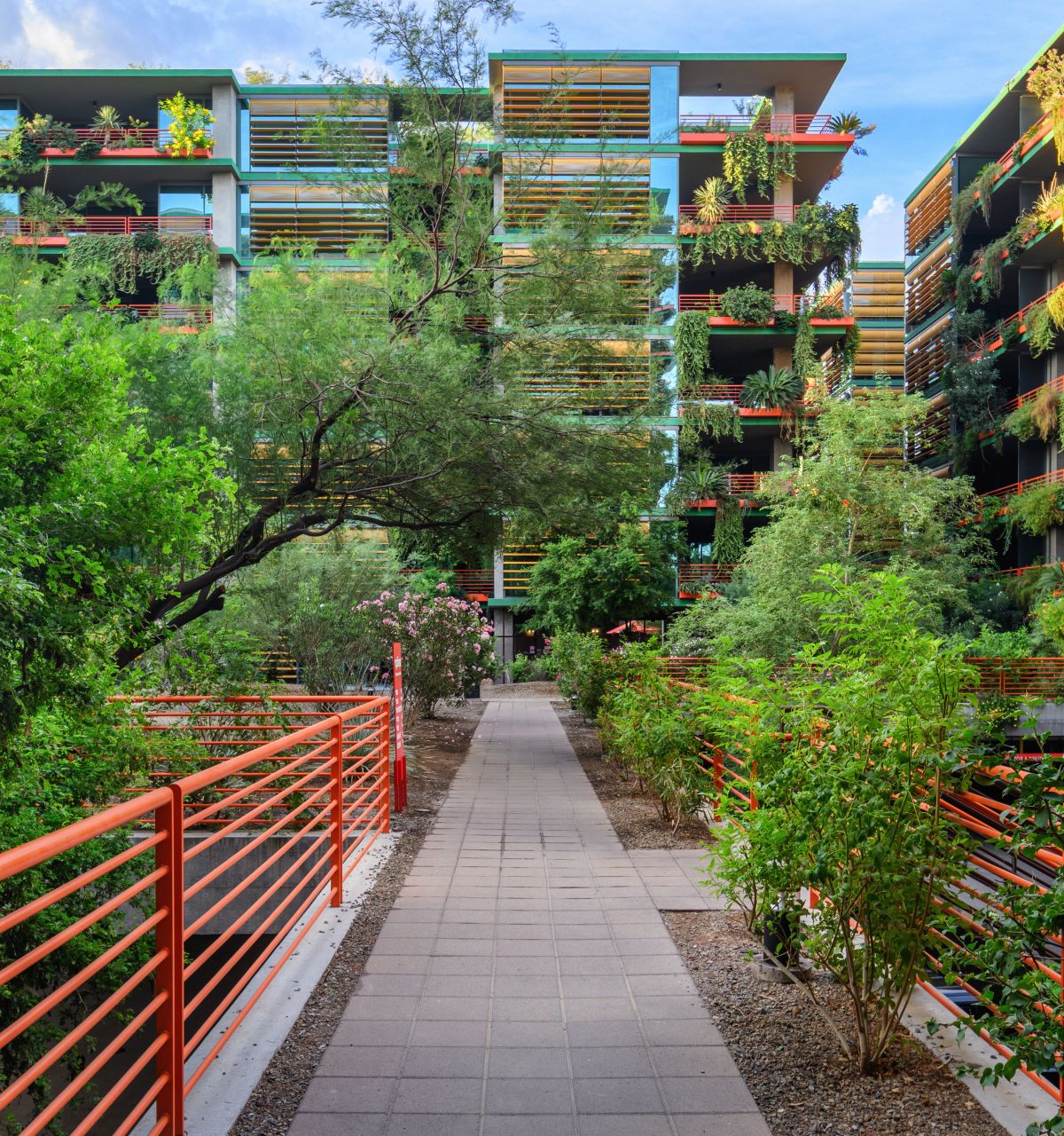Pathway with red railings leads to modern apartments, offering urban living and walkability amid lush greenery and stylish plant decor.