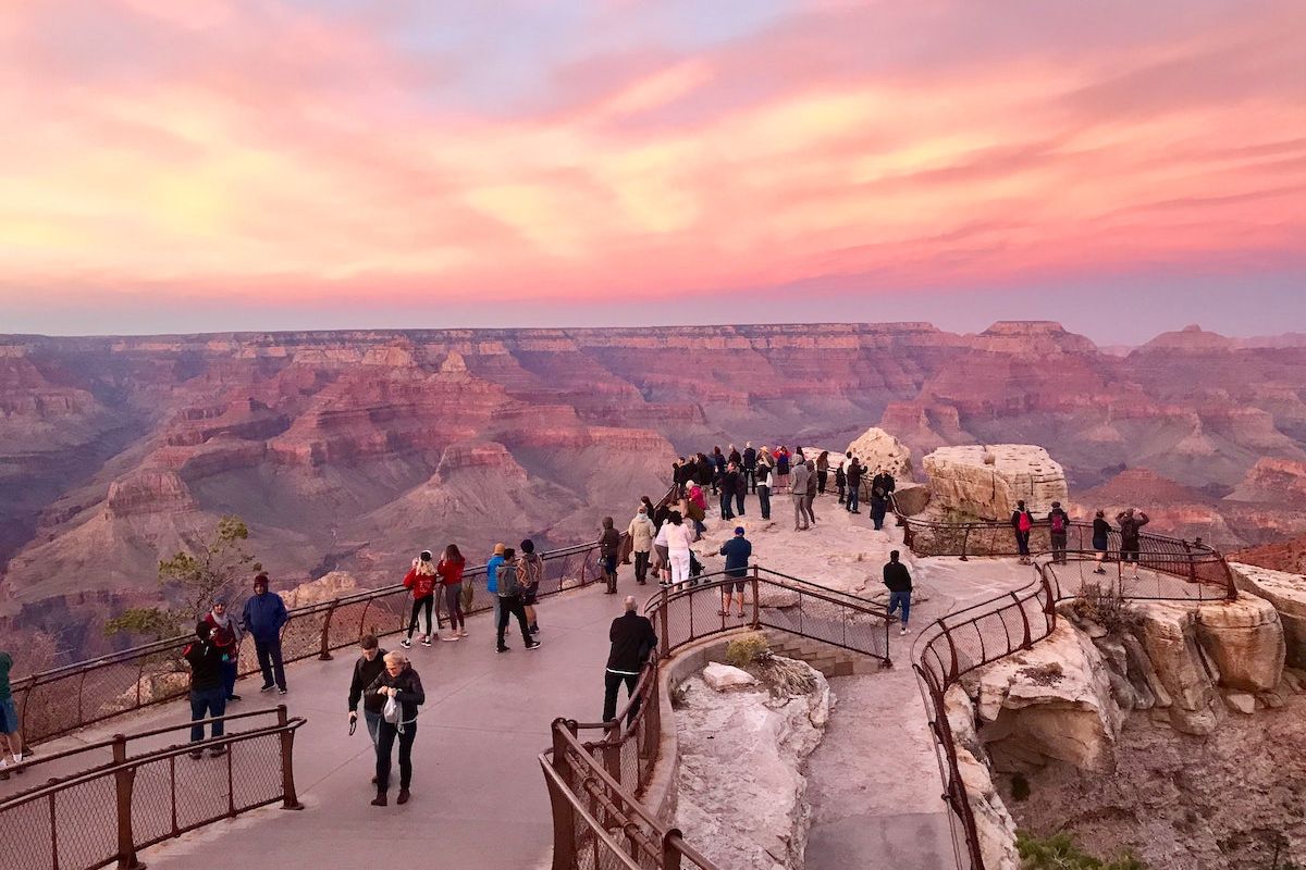 People gather at a Grand Canyon viewpoint at sunset, a favorite for day trips from Phoenix and Scottsdale under a colorful pink and orange sky.