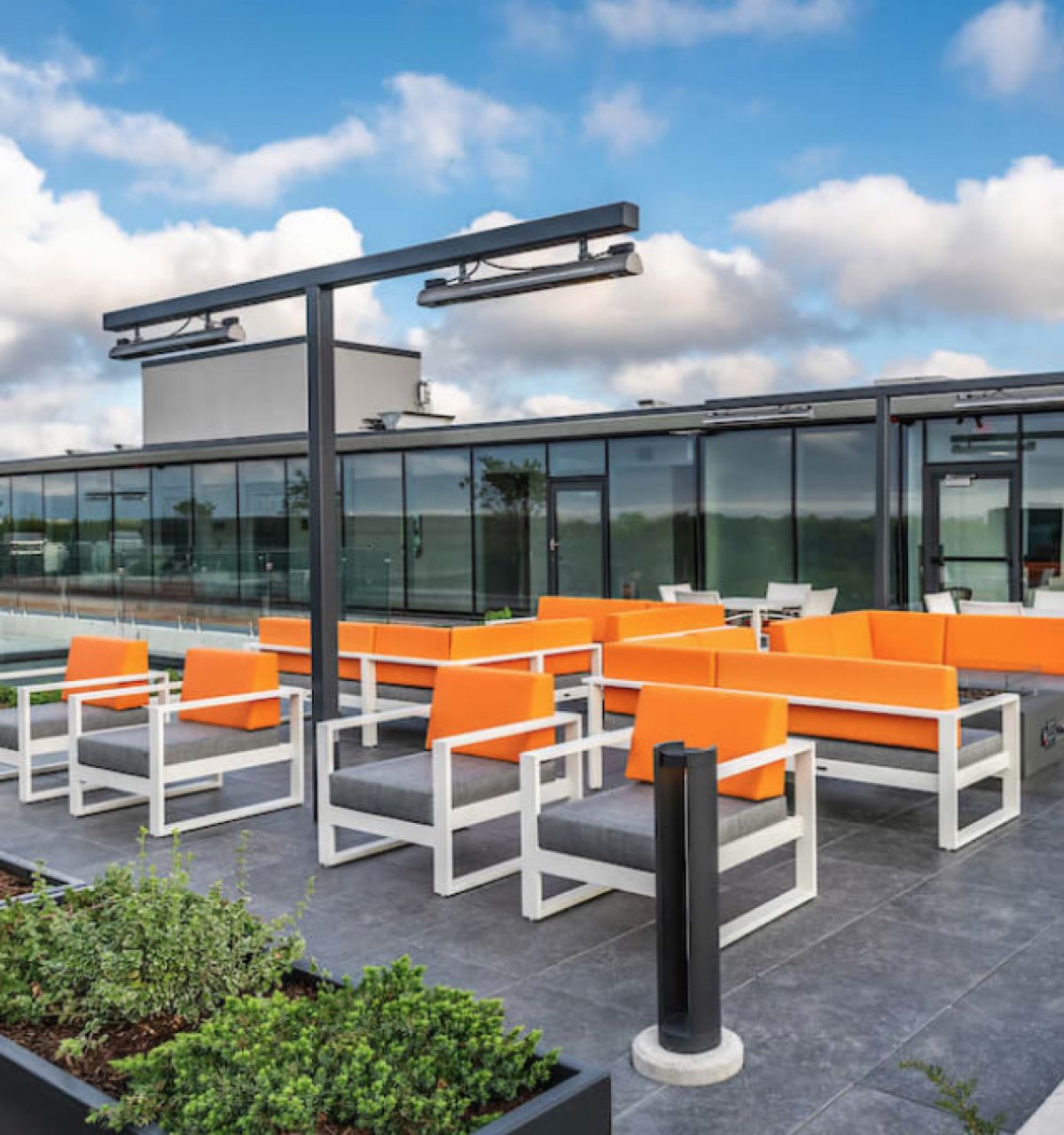 Rooftop patio at Optima Sonoran Village with bright orange seating, modern decor, greenery, and green roofs under a cloudy sky.