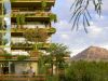 Modern apartment building with lush balcony plants, mountain in background, and person walking below.