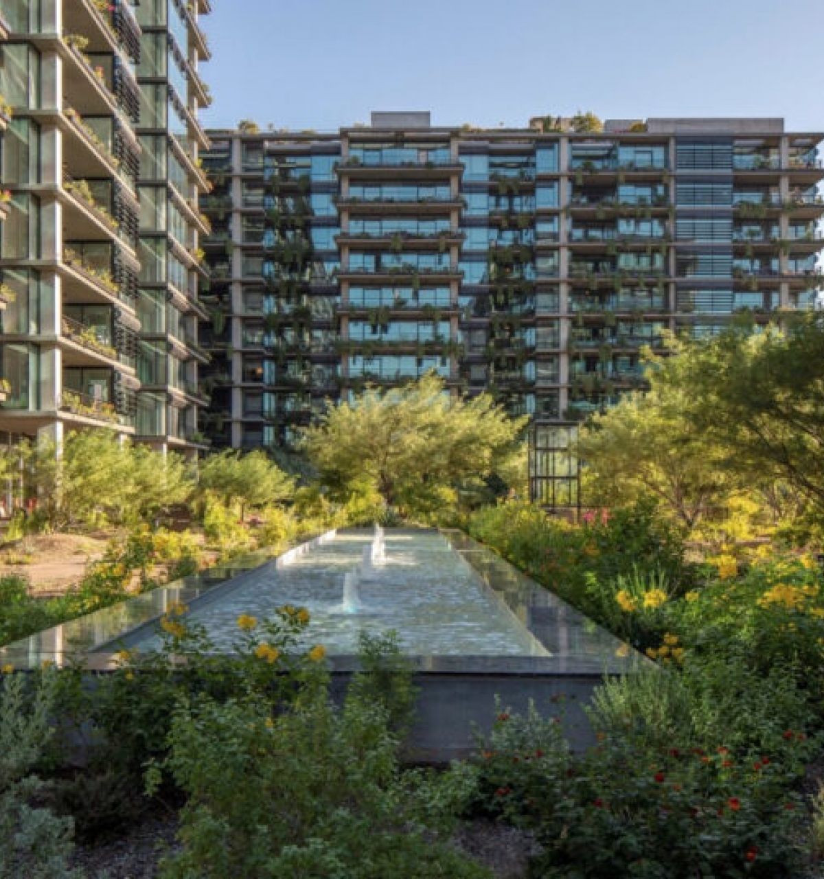 Modern apartment buildings with glass balconies, lush gardens, natural stone accents, and a long reflecting pool in the center.