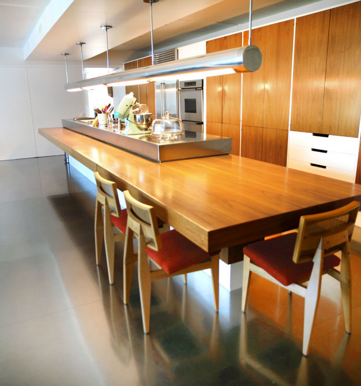 Modern Phoenix kitchen with a long wooden island, three chairs, sleek Mid-Century Modern cabinets, and shiny polished floors.