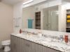Modern bathroom design with a marble countertop, double sinks, large mirror, toilet, and wooden cabinets under bright lighting.