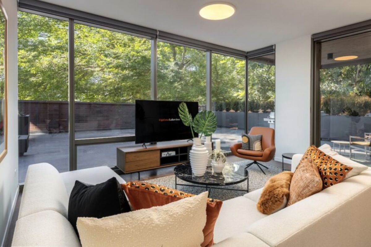 Modern living room with large windows, white sectional sofa, TV, and views of greenery that blend indoor comfort with outdoor living spaces.