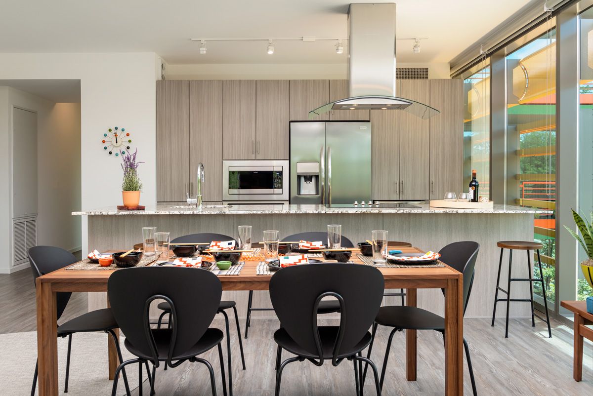 Modern kitchen with a wooden dining table set, black chairs, and a counter with stainless steel appliances at Optima Sonoran Village apartments.
