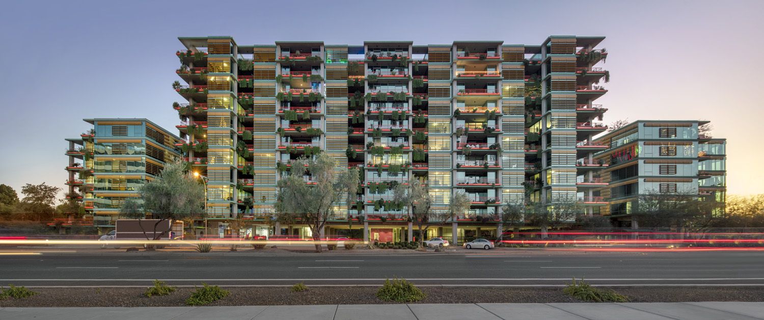 Modern multi-story apartment building at sunset, with balconies and greenery—Optima Sonoran Village blends climate design for the desert climate.