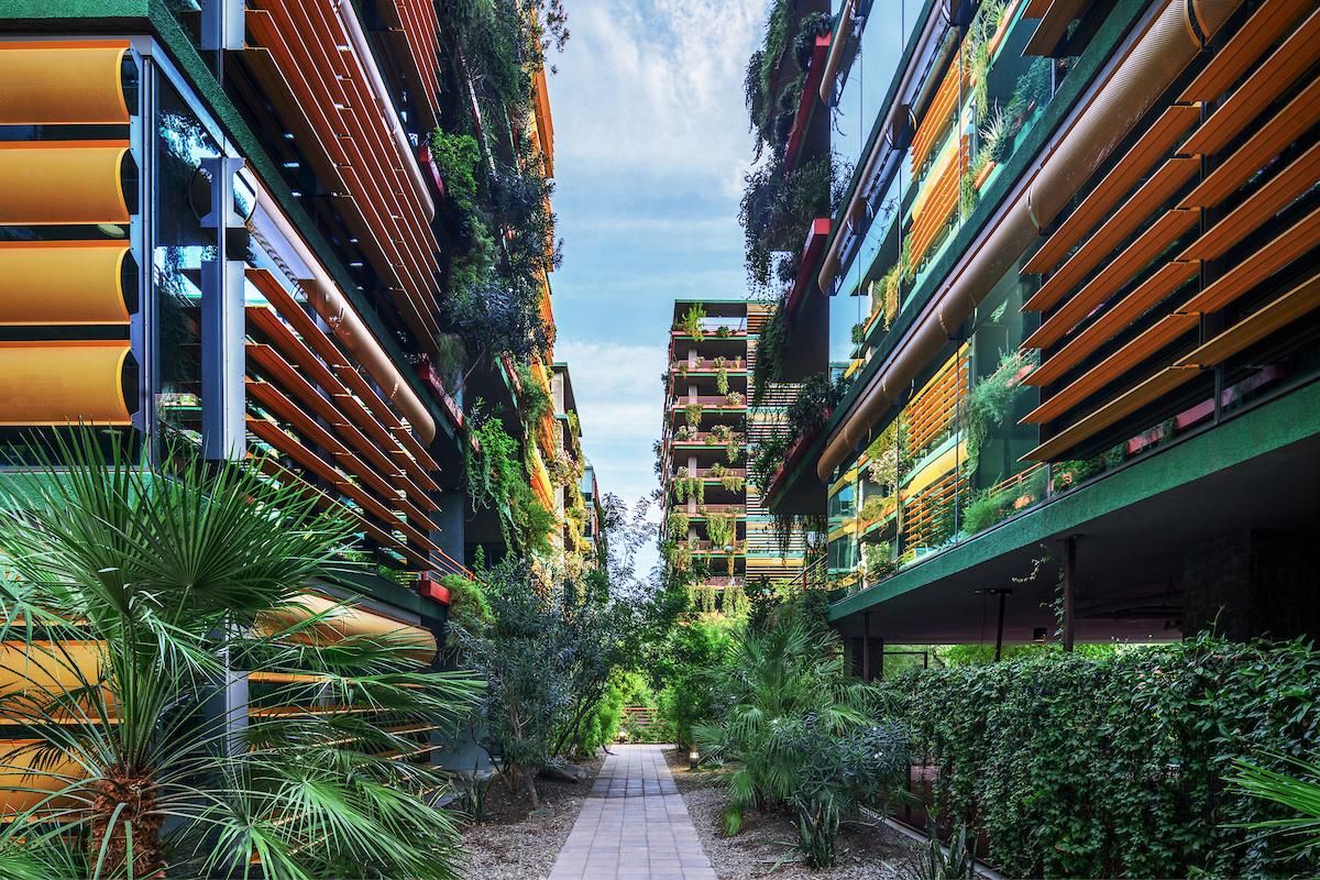 A walkway at Optima Sonoran Village with orange sunshades, lush biophilic design, and greenery on balconies and ground level.
