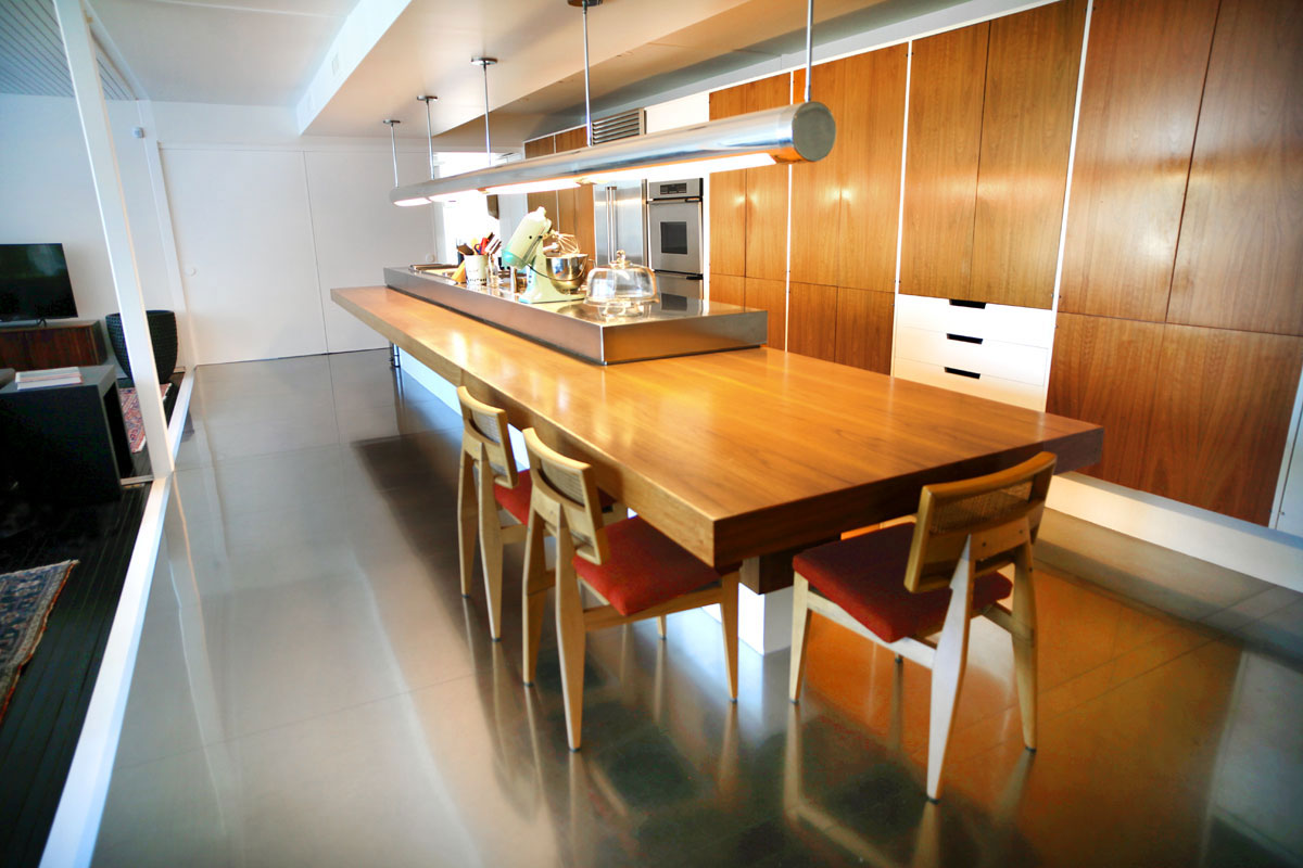 Modern Phoenix kitchen with a long wooden island, three chairs, sleek Mid-Century Modern cabinets, and shiny polished floors.