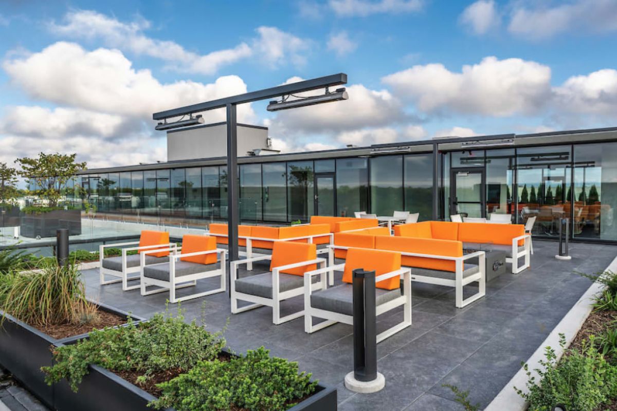Rooftop patio at Optima Sonoran Village with bright orange seating, modern decor, greenery, and green roofs under a cloudy sky.