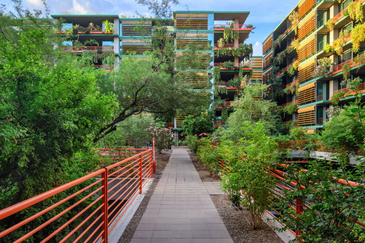 Pathway with red railings leads to modern apartments, offering urban living and walkability amid lush greenery and stylish plant decor.