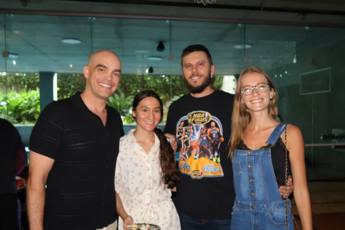 Four people indoors, three smiling at the camera; one holding a plate of food—enjoying Optima Connect perks by large windows.