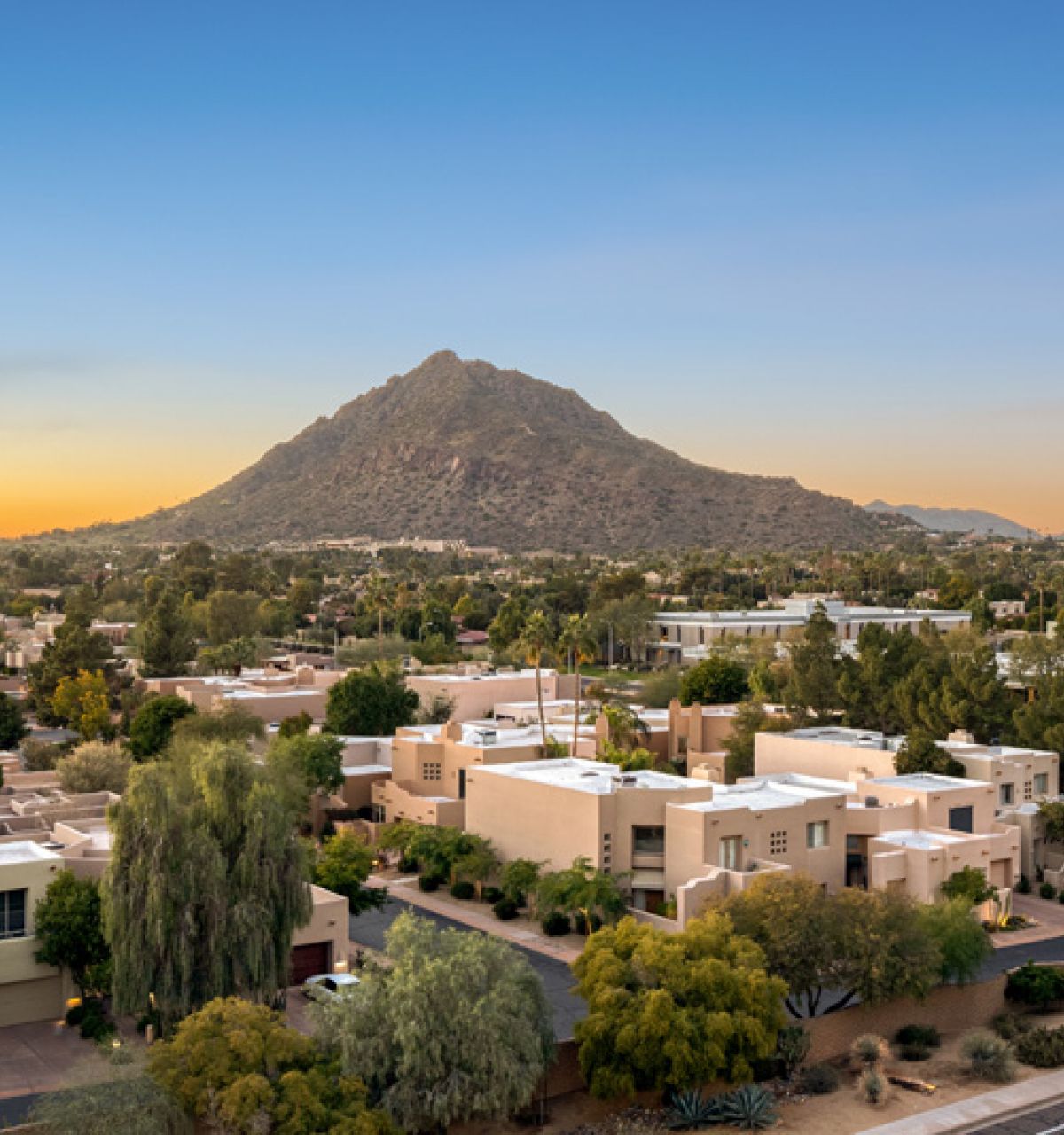 View from Optima Sonoran Village apartment rooftop of suburban neighborhood with desert landscaping and a mountain backdrop at sunset.