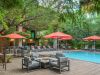 Outdoor pool area at Optima Sonoran Village features lounge chairs, orange umbrellas, and year-round outdoor living amid lush green trees.