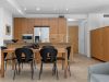 Modern Optima kitchen design and dining area with wooden cabinets, black chairs, and neutral tiled flooring for a stylish home.