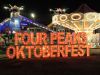 A glowing "Four Peaks Oktoberfest" sign shines at Tempe Beach Park, set against the backdrop of lively carnival rides at night.