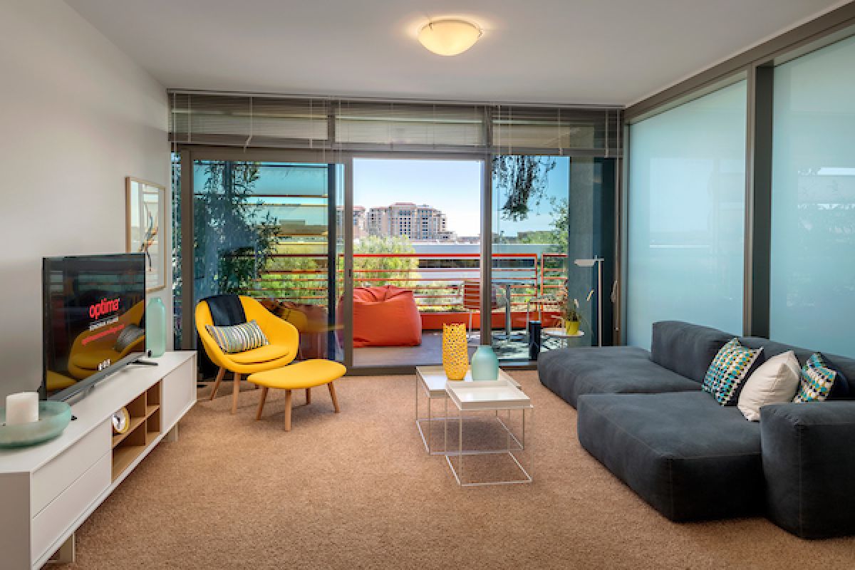 Modern living room in Scottsdale luxury apartments with gray sofa, yellow chair, TV, and balcony offering city views.