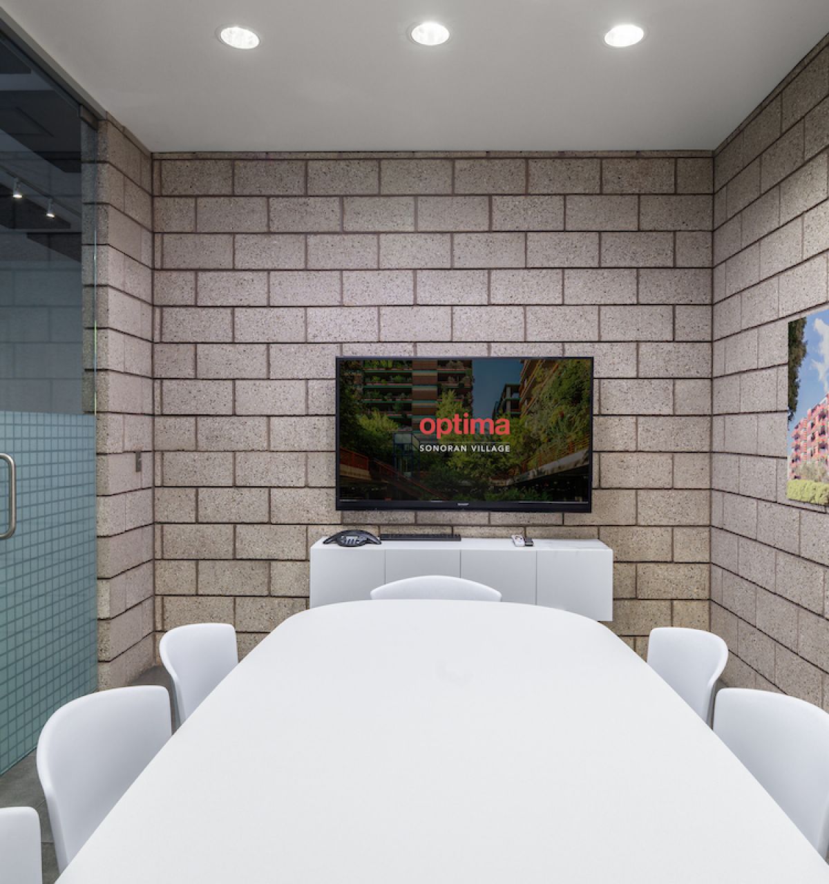 Modern conference room with Optima designs, a white table, chairs, TV, and building photos—ideal for meetings or remote work.