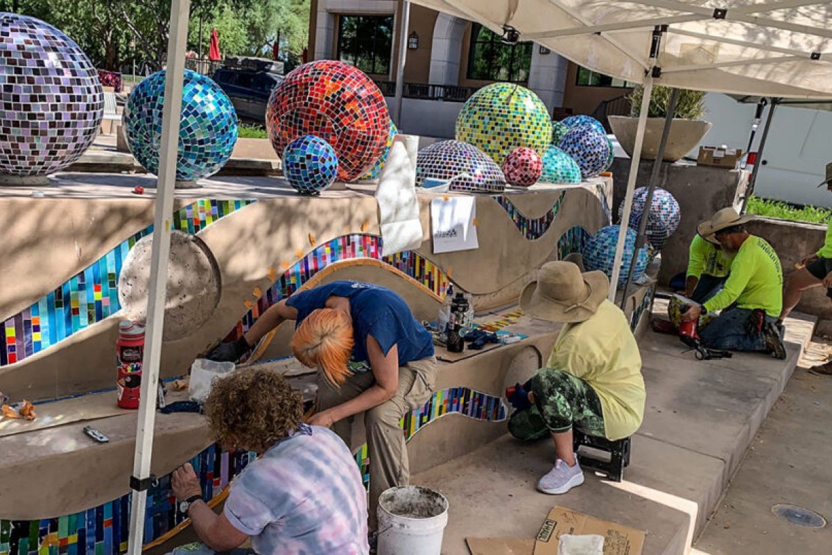 People creating a colorful mosaic mural on outdoor steps for Scottsdale Public Art, under a white canopy.
