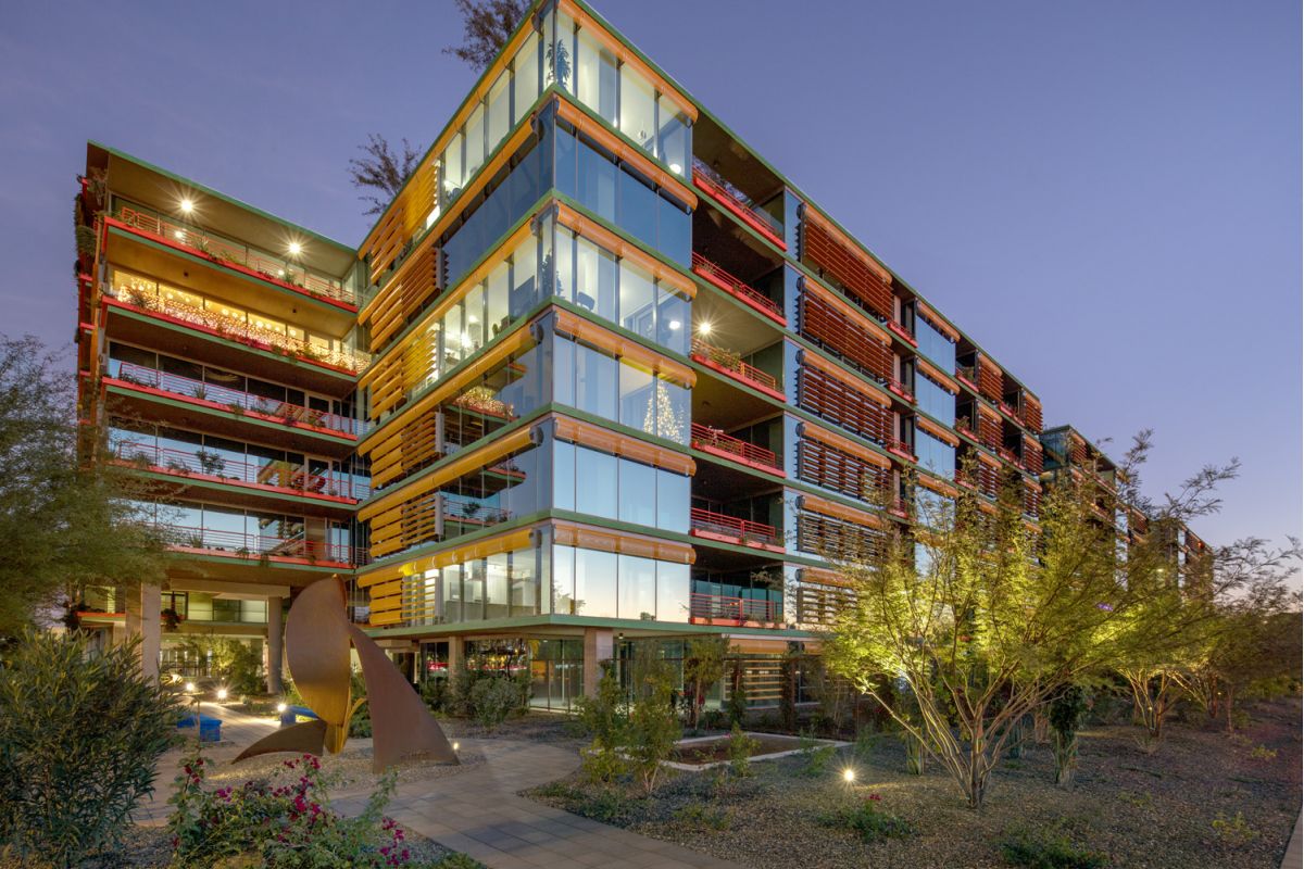 Modern glass and steel building with red accents, a home environment designed to enhance sleep quality, surrounded by desert landscaping at sunset.