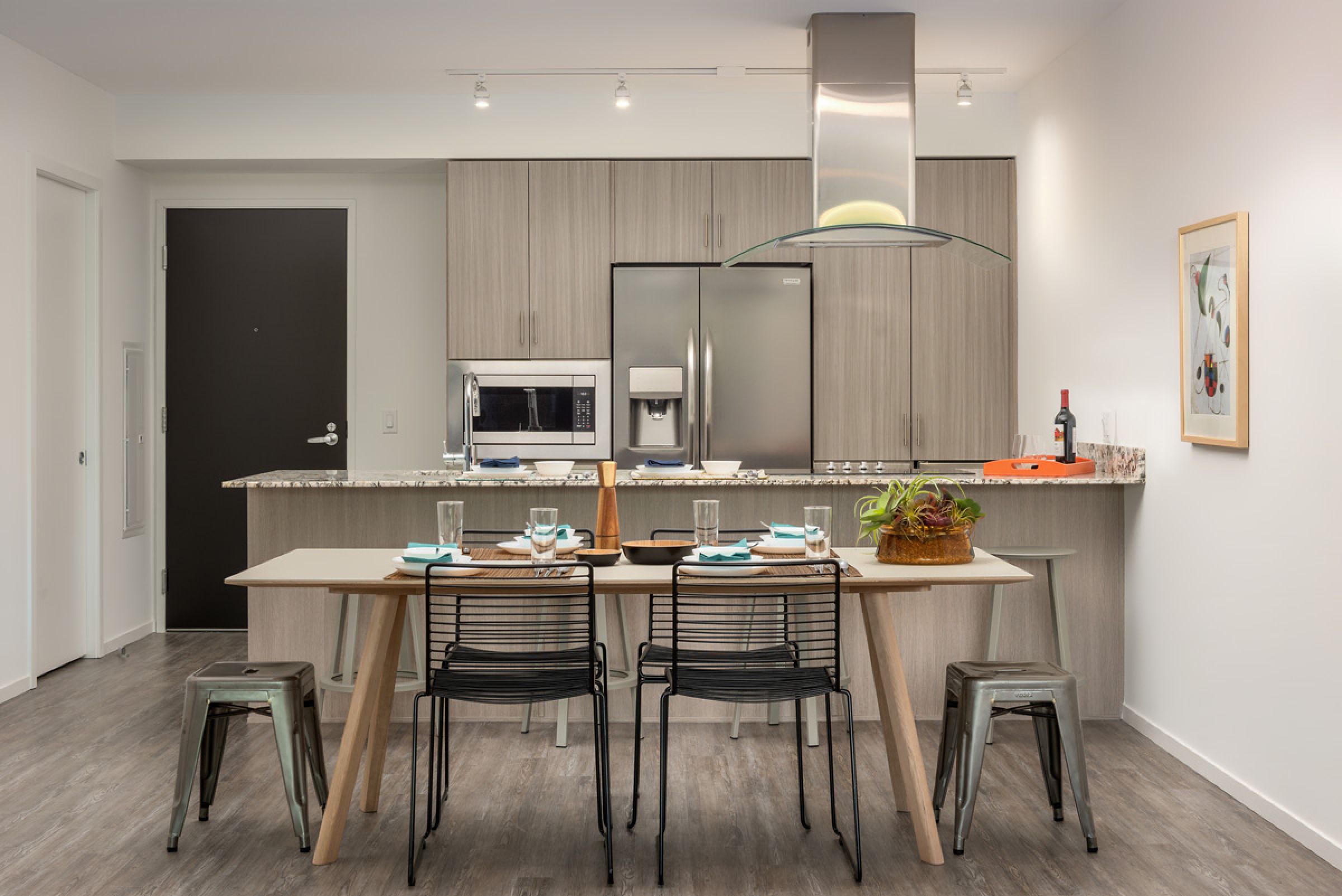 Optima Sonoran Village apartment Modern kitchen with dining table, chairs, barstools, stainless steel appliances, and a plant centerpiece.