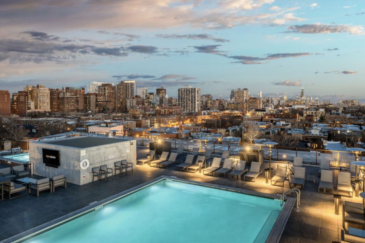 A rooftop pool with lounge chairs overlooks a city skyline at sunset, showcasing the benefits of living with a view.