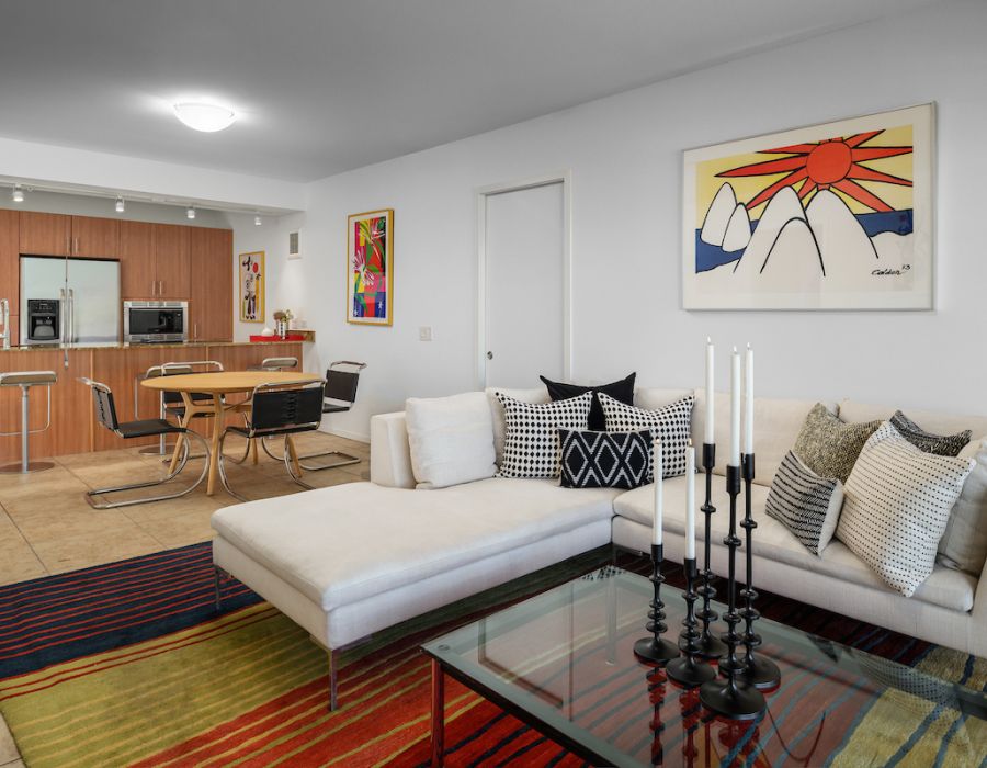 Modern open-plan living and dining area with white sectional sofa, colorful rugs, and art on the walls.