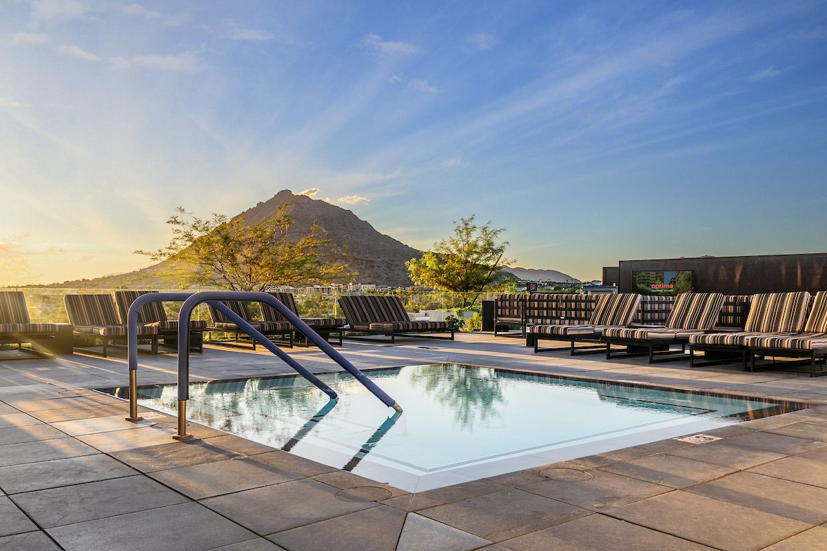 Rooftop pool with striped lounge chairs and a mountain in the background at sunset.