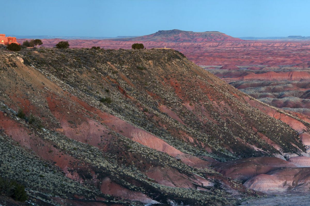 A building sits atop a colorful, layered cliff in Petrified Forest National Park's vast, painted desert landscape at sunset.