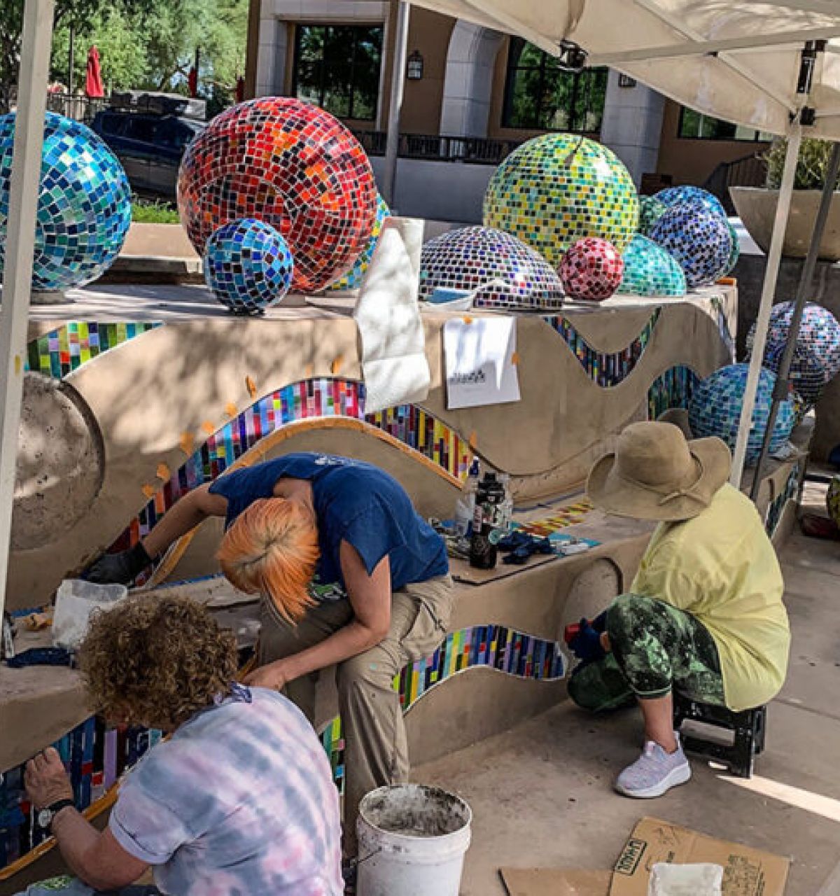 People creating a colorful mosaic mural on outdoor steps for Scottsdale Public Art, under a white canopy.