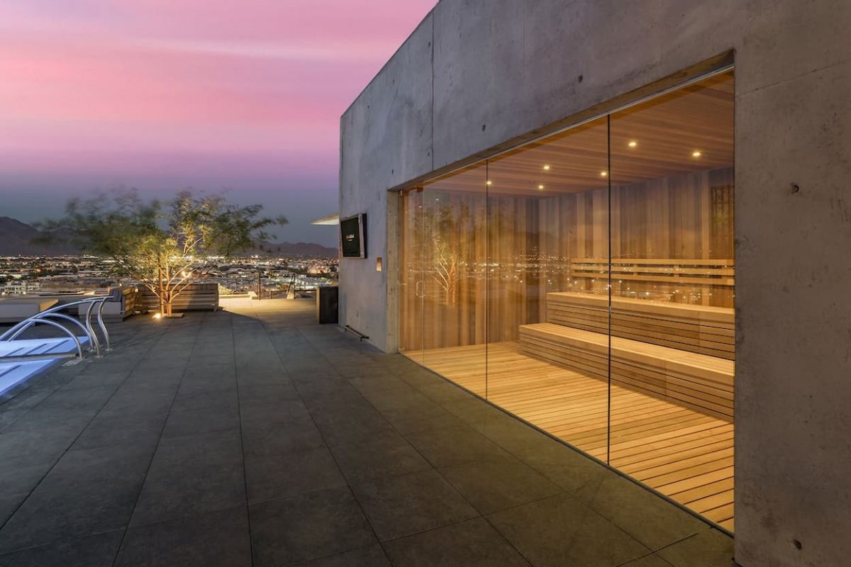Rooftop sauna with glass walls at Optima Communities, featuring well-being amenities, city views, and a lit pool at sunset.