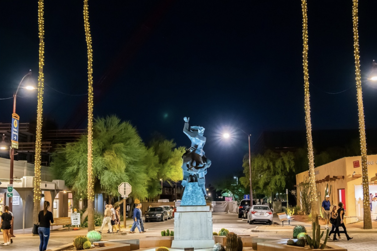 Nighttime street scene with a bronze statue in a roundabout, glowing palm trees, and Scottsdale ArtWalk ambiance.