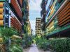 Two people walk between pet-friendly, modern green buildings at Optima Sonoran Village, surrounded by orange sunshades and lush plants.