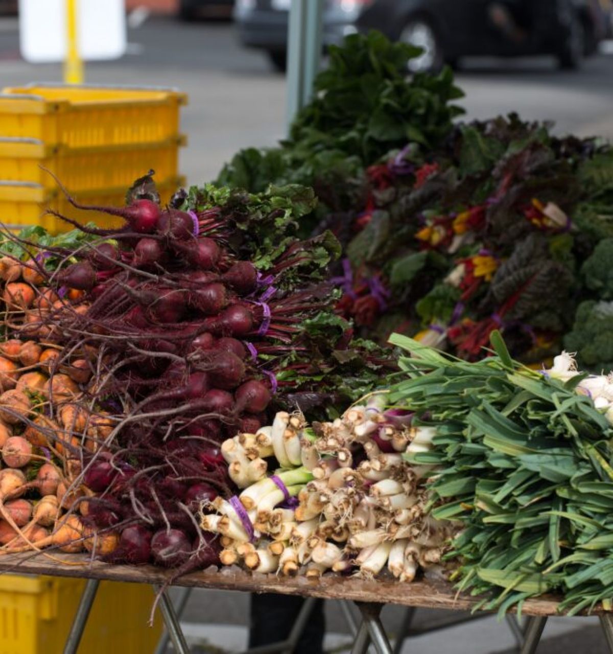 Fresh root vegetables and greens at the Scottsdale Farmers Market, capturing the vibrant local flavor with yellow crates in the background.