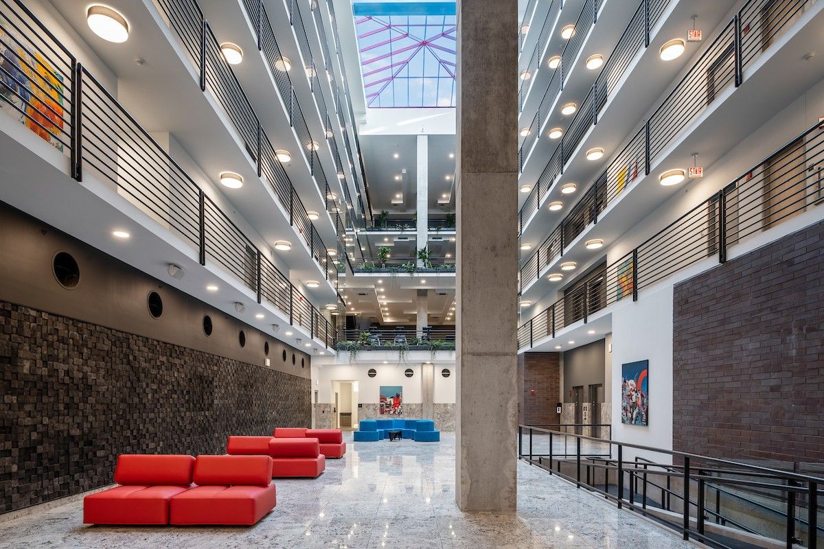 Modern atrium with red couches, balconies, and a skylight ceiling filling the space with natural light and sunlight health benefits.