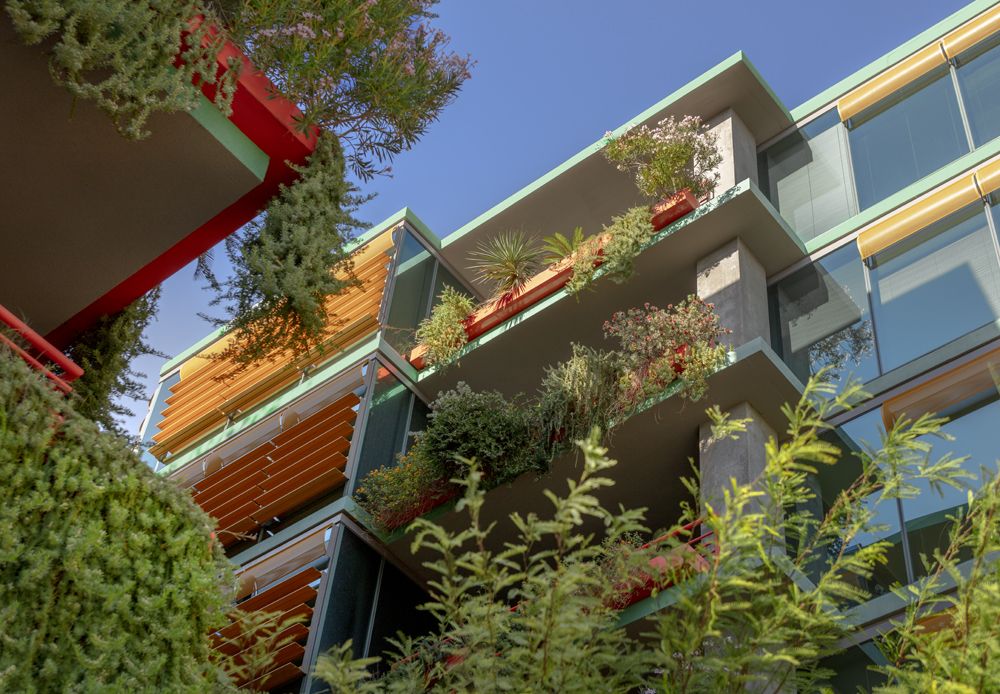 Optima Sonoran Village apartments modern building with balconies covered in lush greenery and plants, set against a clear blue sky.