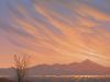 Desert landscape at sunset with glowing city lights and colorful clouds streaking across the sky.