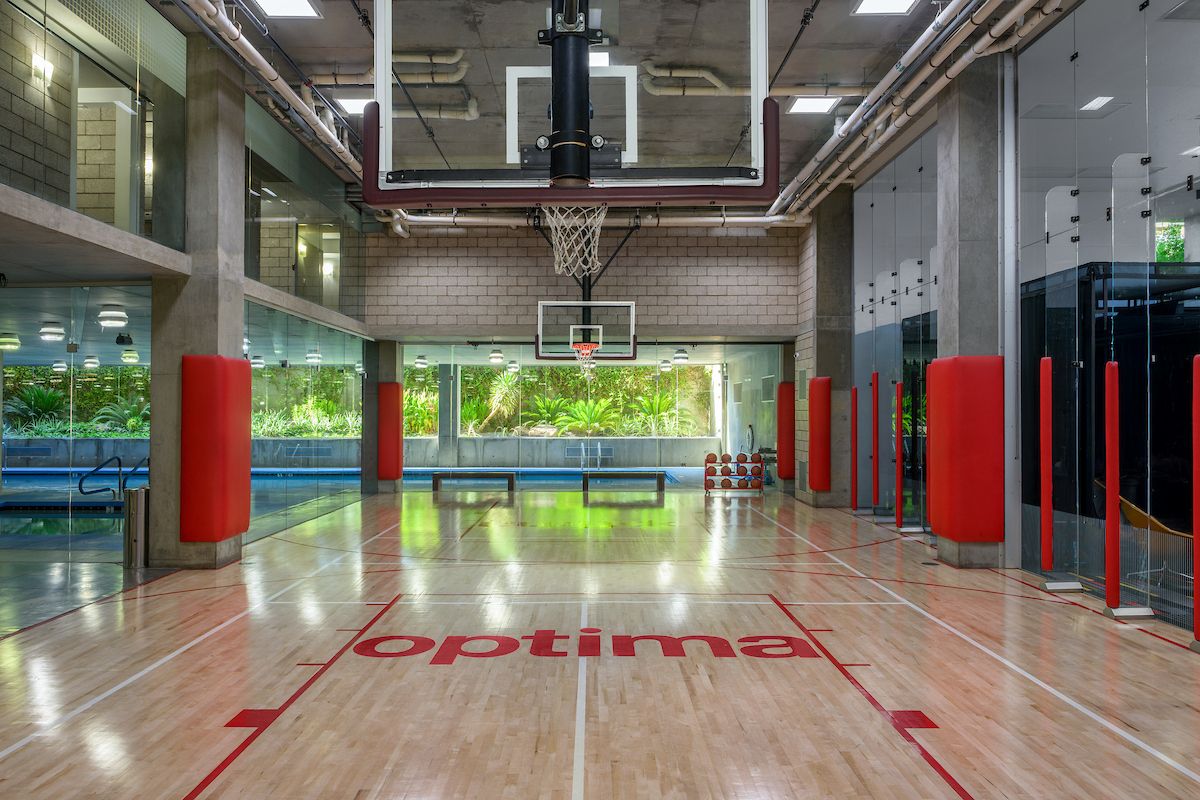 Indoor basketball court with "optima" on the floor, glass walls, and a pool—ideal for morning rituals or productive spaces.
