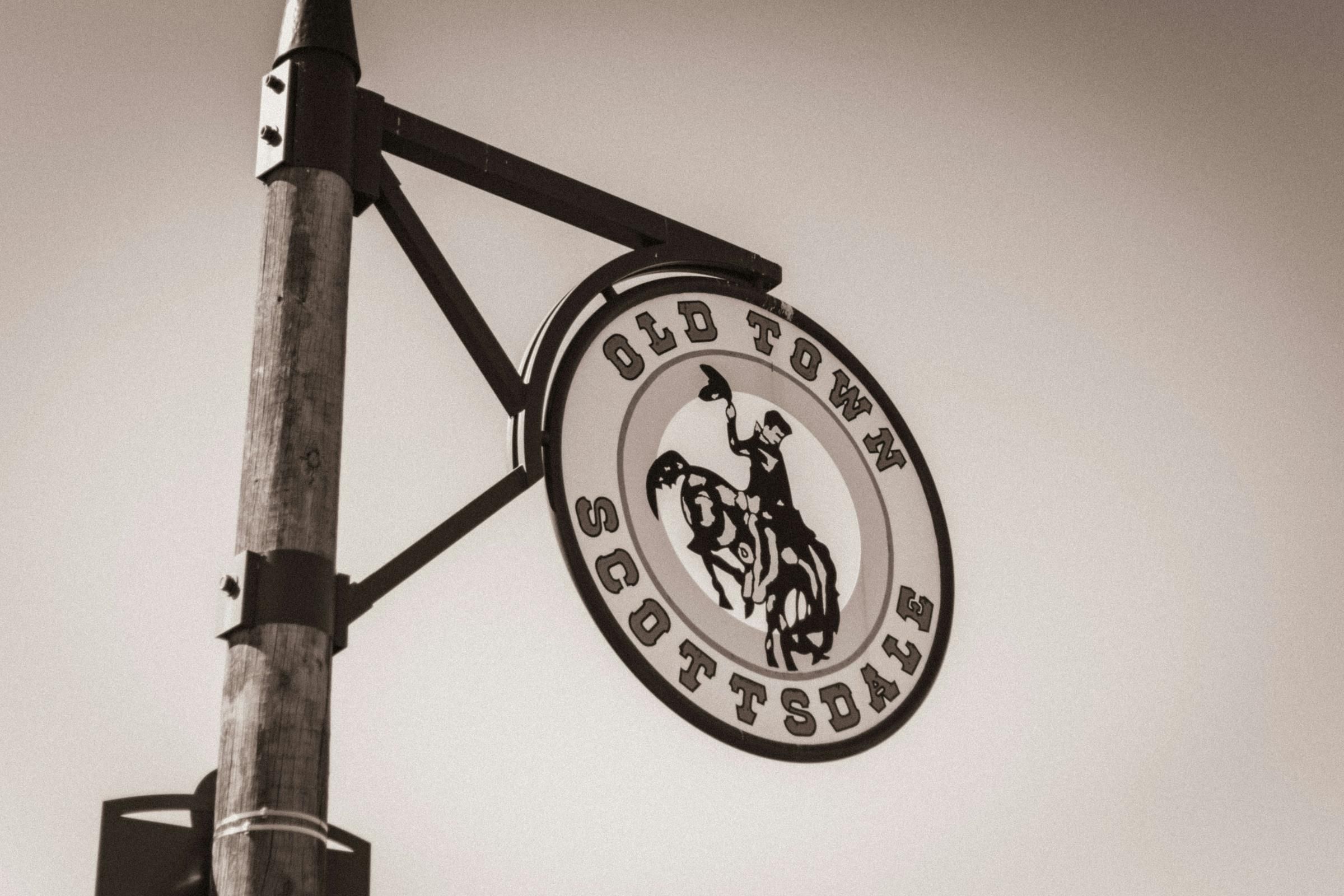 Sign for Old Town Scottsdale featuring a cowboy on a bucking horse, mounted on a wooden pole near Optima Sonoran Village apartments.
